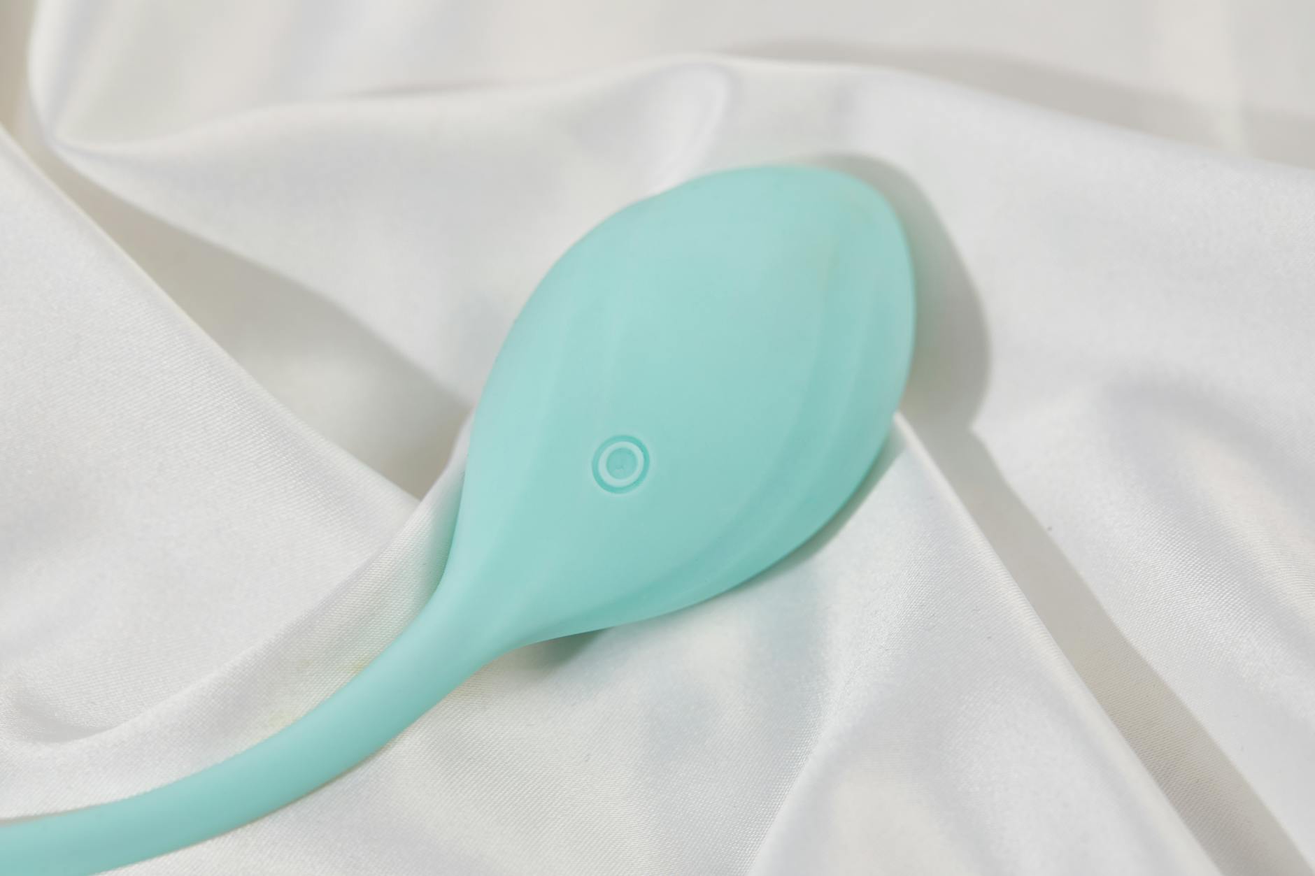 Ein stilvoller türkisfarbener Vibrator auf glatter weißer Seide, perfekt für Lifestyle-Aufnahmen.