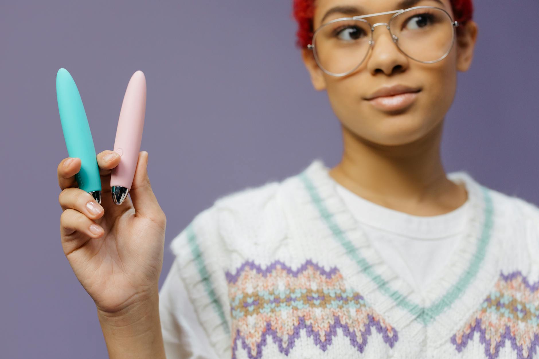 Frau mit Brille hält zwei farbige Silikonvibratoren nachdenklich