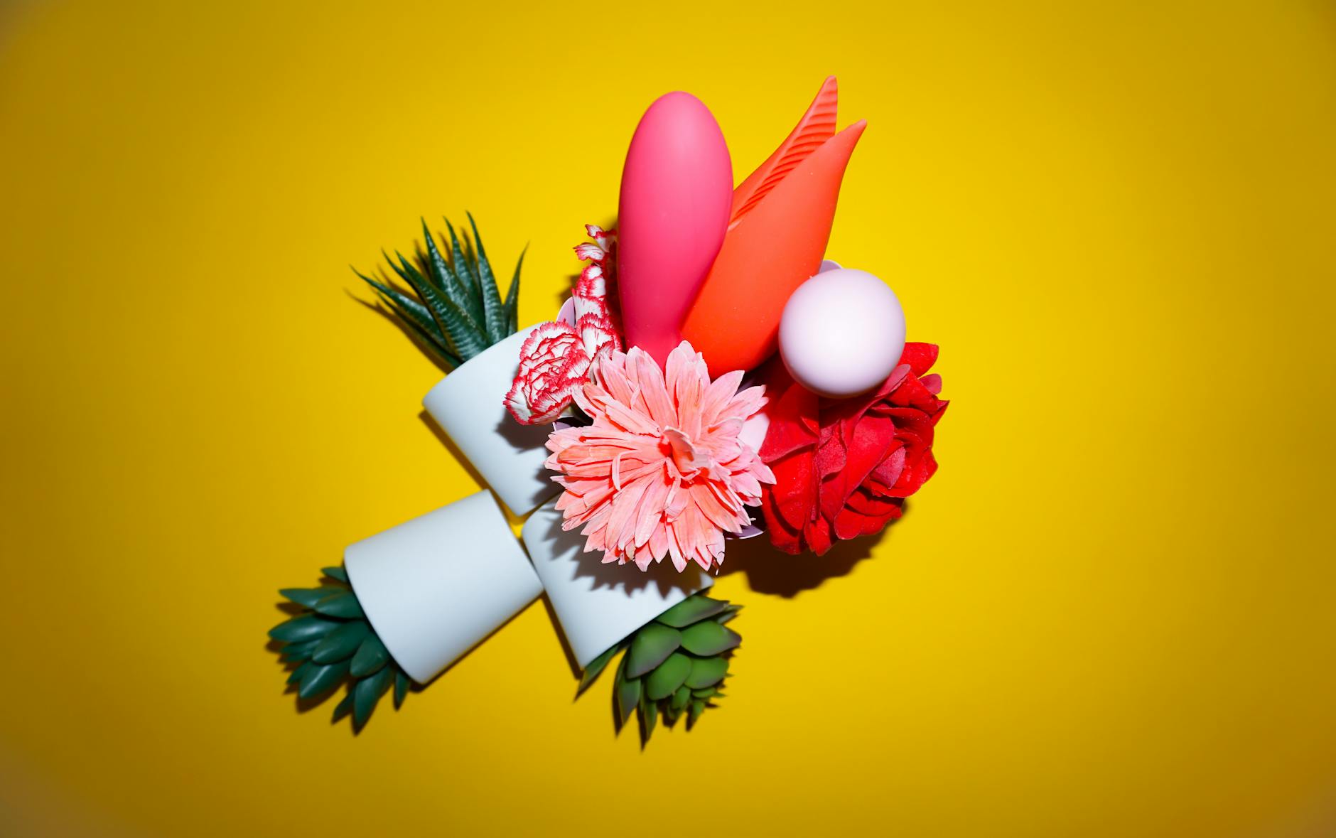 Bunte Anordnung von Blumen und abstrakten Objekten auf gelbem Hintergrund, symbolisierend Vitalität und Freude