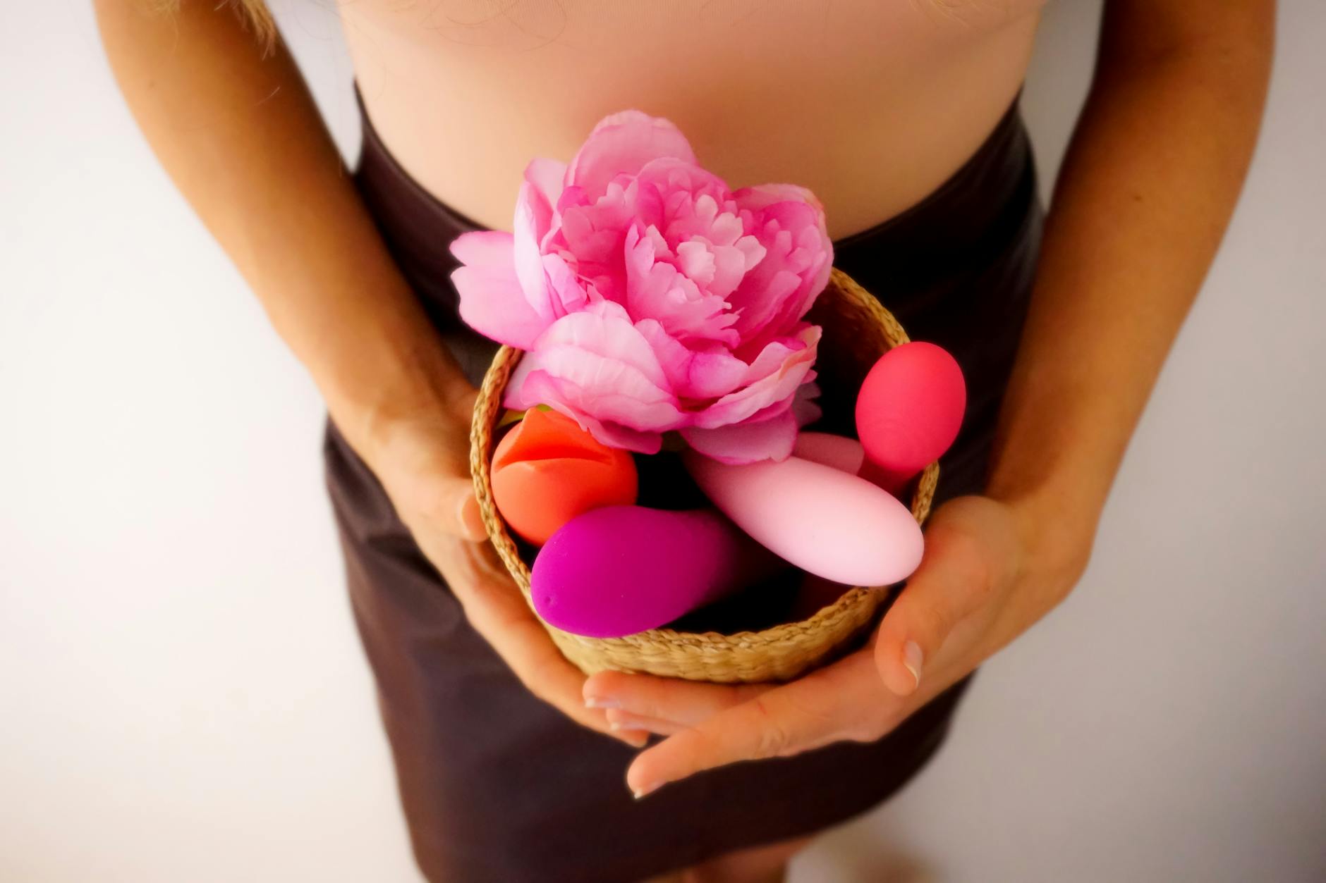 Eine Hand hält einen orangefarbenen Vibrator vor einem minimalistischen violetten Hintergrund.